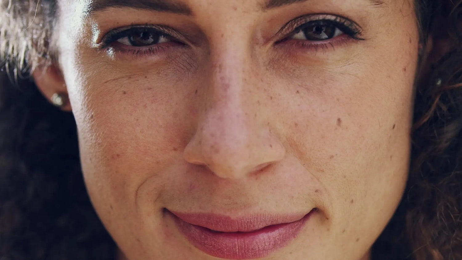 Close-up van een glimlachende vrouw met sproeten en kleine pigmentvlekjes op wangen en neus