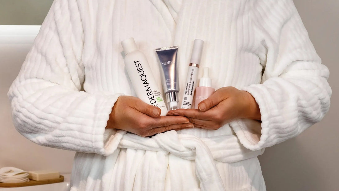 Vrouw in witte badjas houdt vier skincareproducten met werkzame stoffen in haar handen