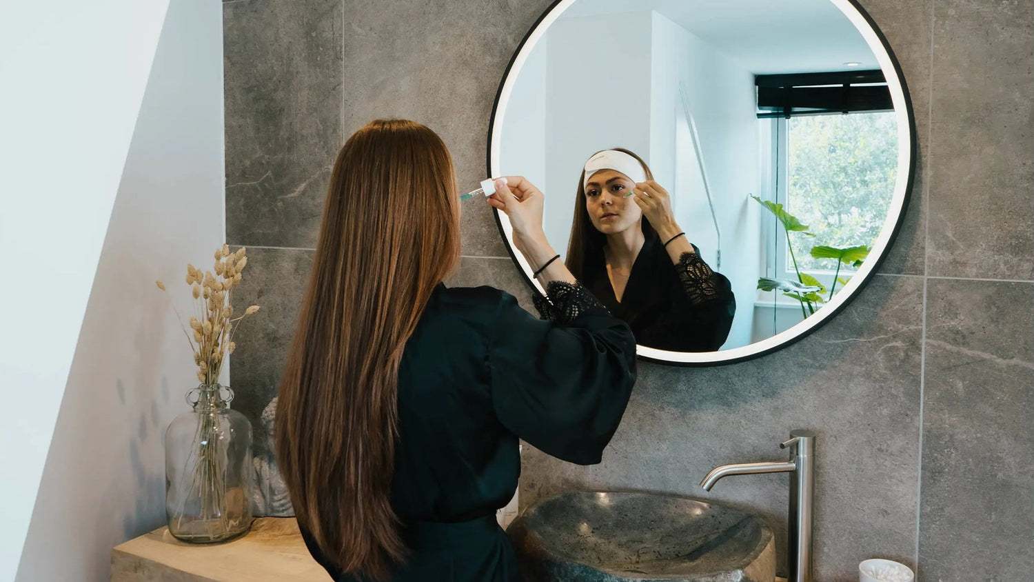 Vrouw met haarband brengt voor de spiegel een serum aan op haar droge huid