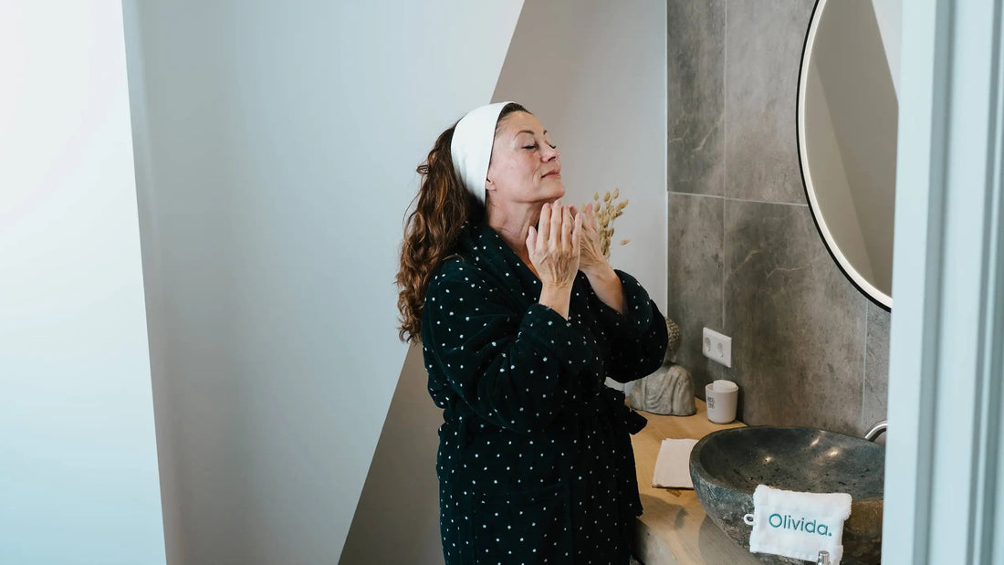 Vrouw in badjas brengt in de badkamer haar nachtcrème aan voor het slapengaan