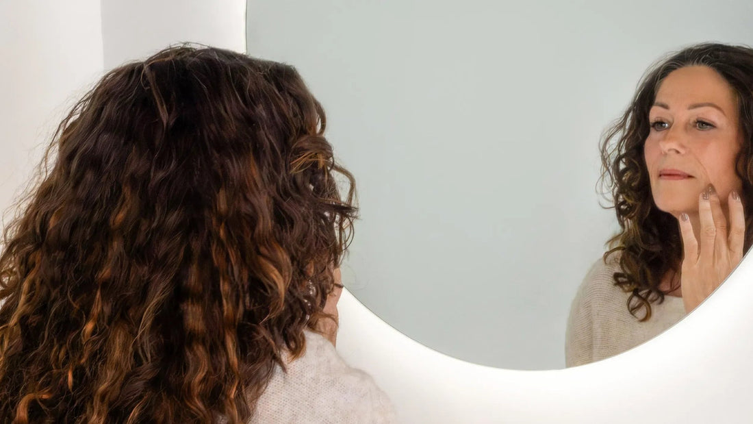 Vrouw bekijkt haar huid in de spiegel voor ze haar crème aanbrengt