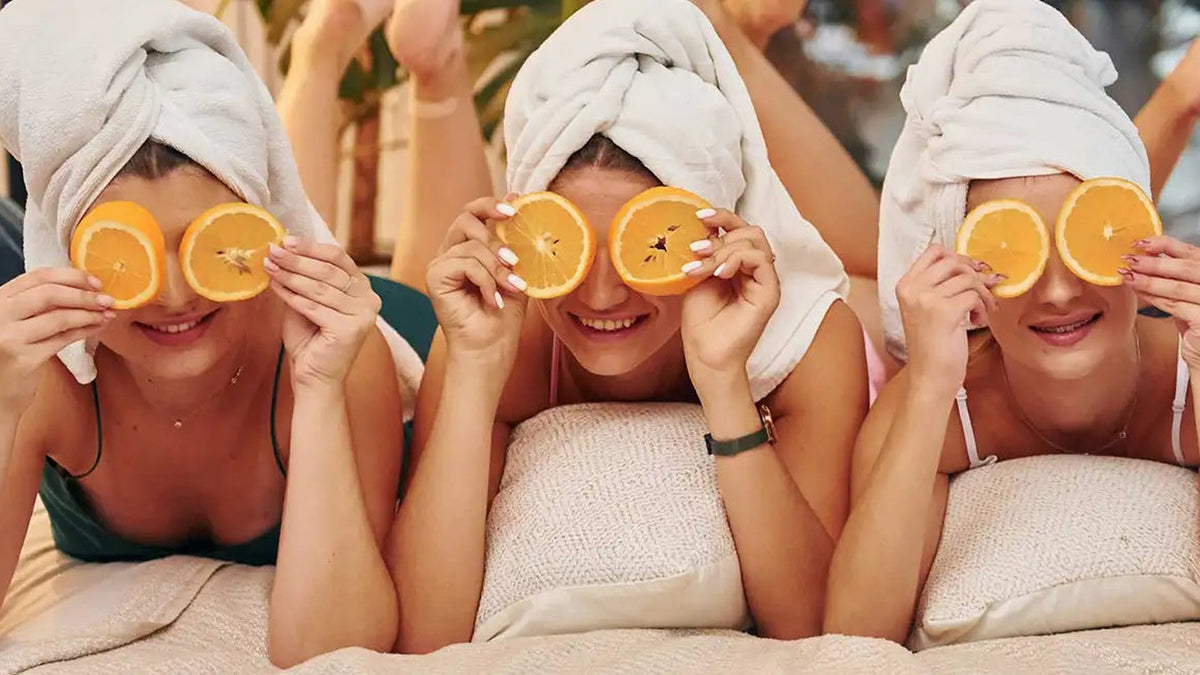 Drie vrouwen met een handdoek om hun haar houden schijfjes sinaasappel voor hun ogen