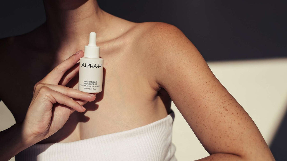 Vrouw houdt een serum bij haar onbedekte hals en decolleté in het zonlicht