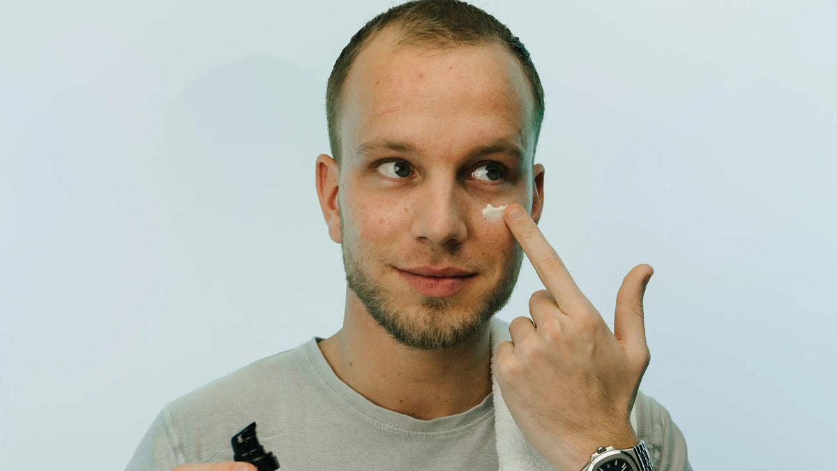 Man brengt met zijn vinger een stipje dagcrème aan onder zijn oog