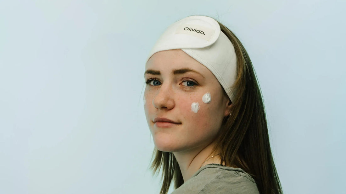 Jonge vrouw met Olivida-haarband en twee dotjes crème op haar wang, klaar voor een milde skincare-routine tijdens de zwangerschap