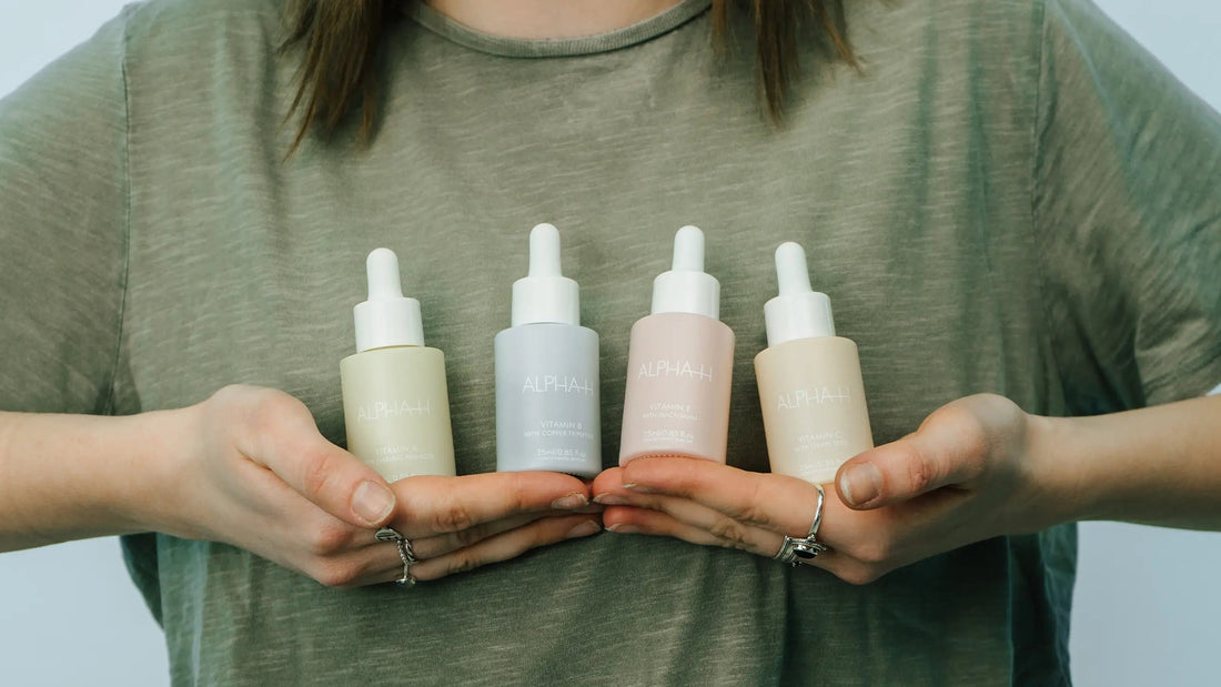 Vrouw in groen T-shirt houdt vier ALPHA-H serums (Vitamin A, B, E en C) in haar handen