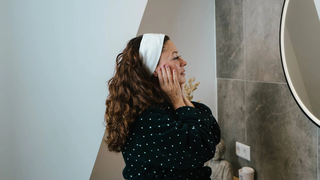 Vrouw met haarband voelt bij de badkamerspiegel aan haar wang